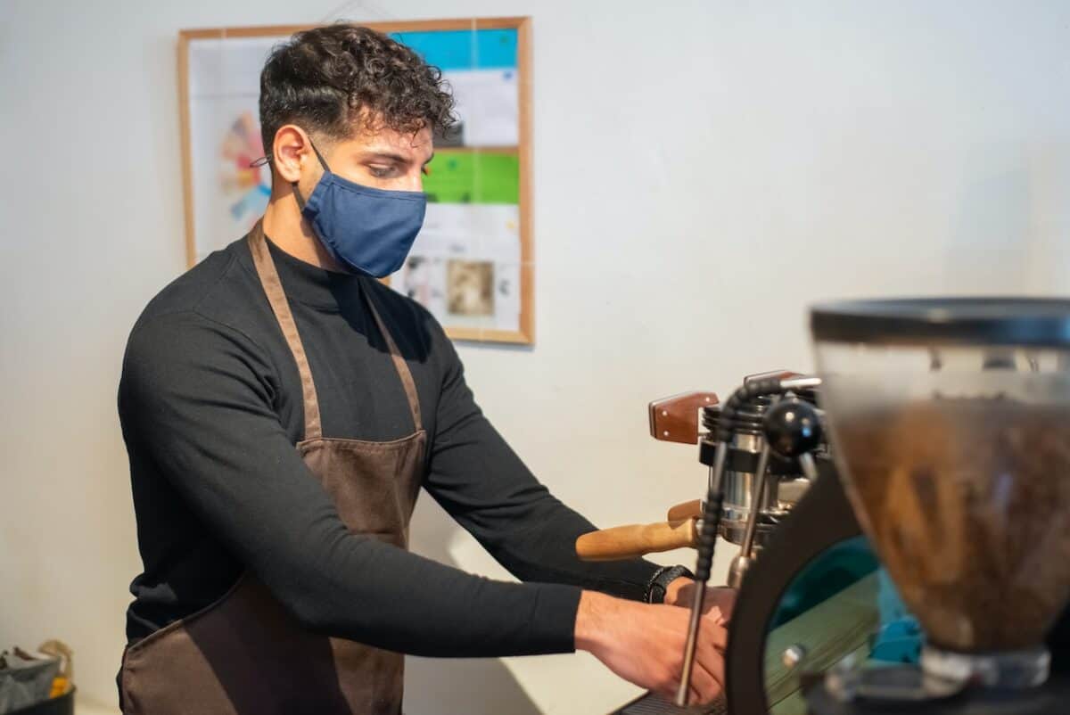 A man wearing black long sleeves and a brown apron fixing a coffee maker