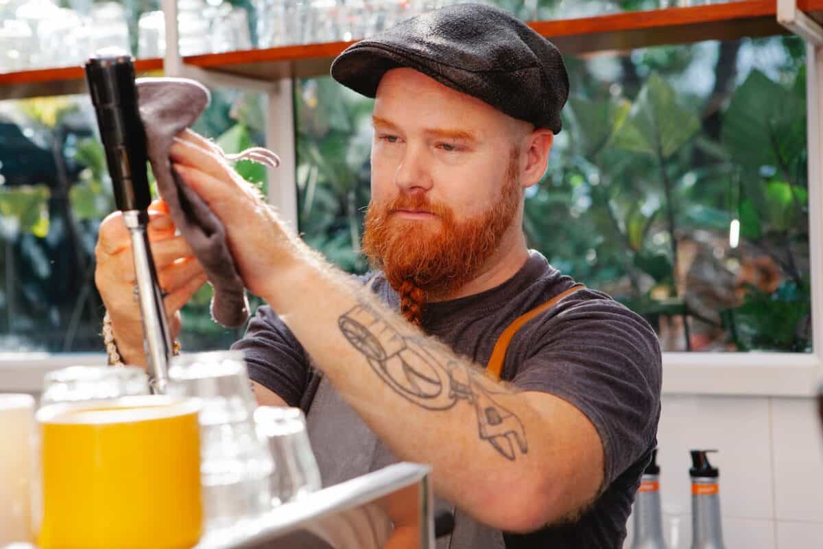 A man in a black t-shirt and apron wiping the coffee maker in the cafe