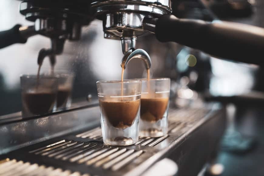 Two small glasses being filled with espresso on a coffee machine