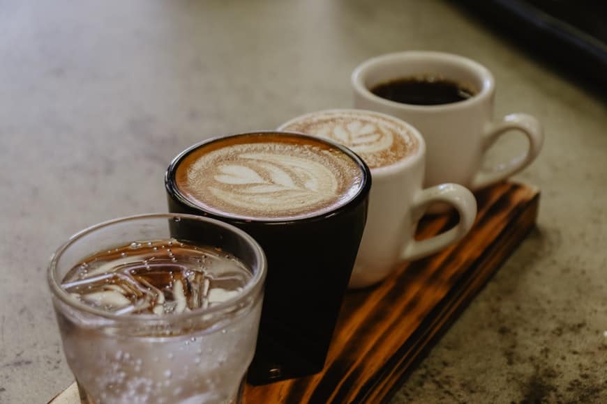 Three cups of coffee and a glass of water with ice were placed on a plank of wood