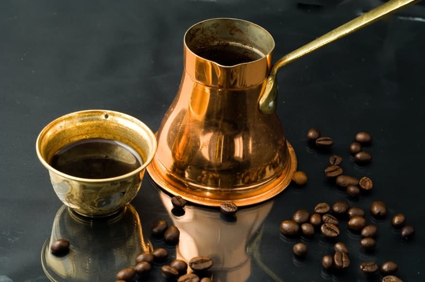 Golden cup with a coffee beside scattered fresh coffee beans on a black surface