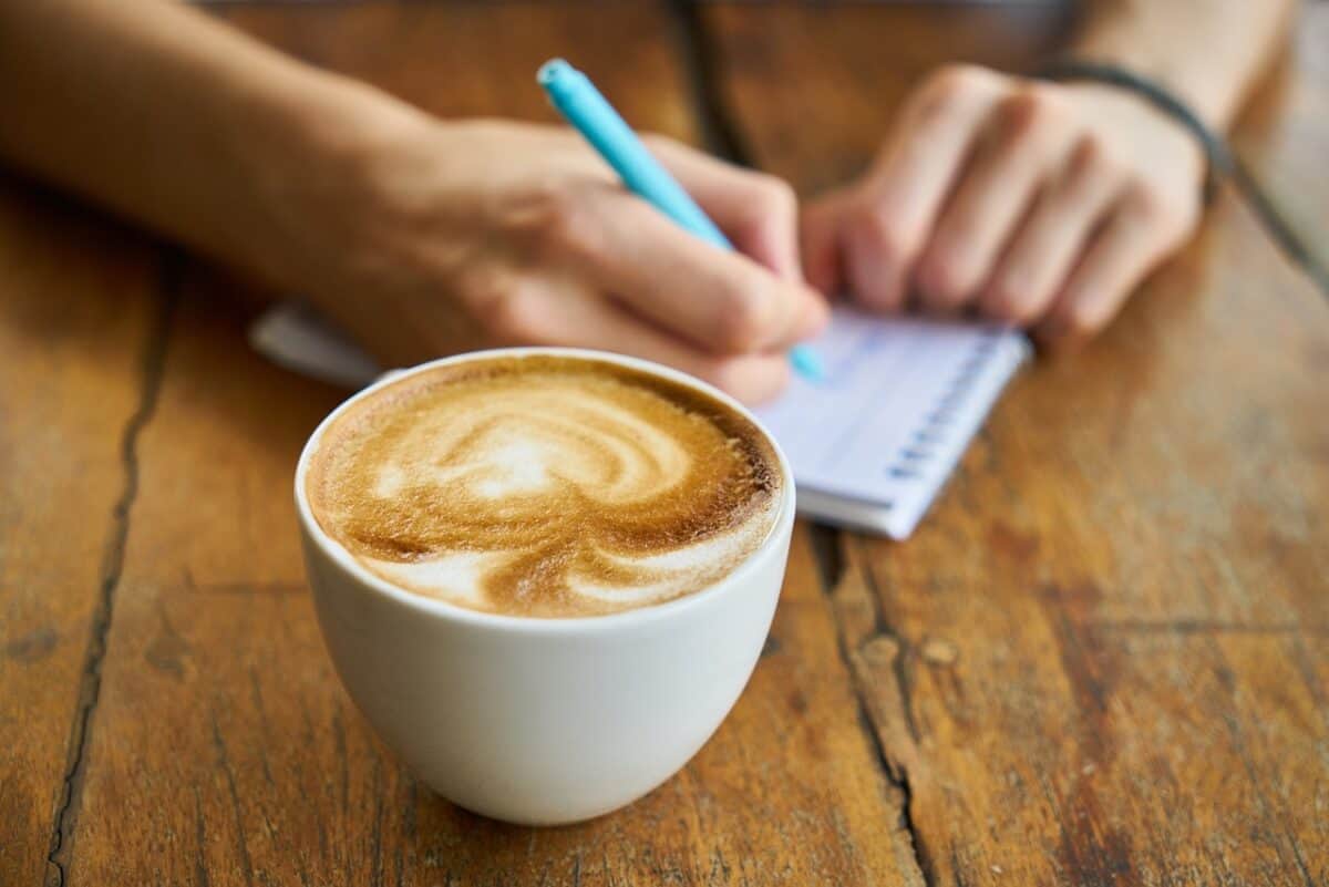 A cup of cappuccino coffee in a white mug placed on a brown wooden table