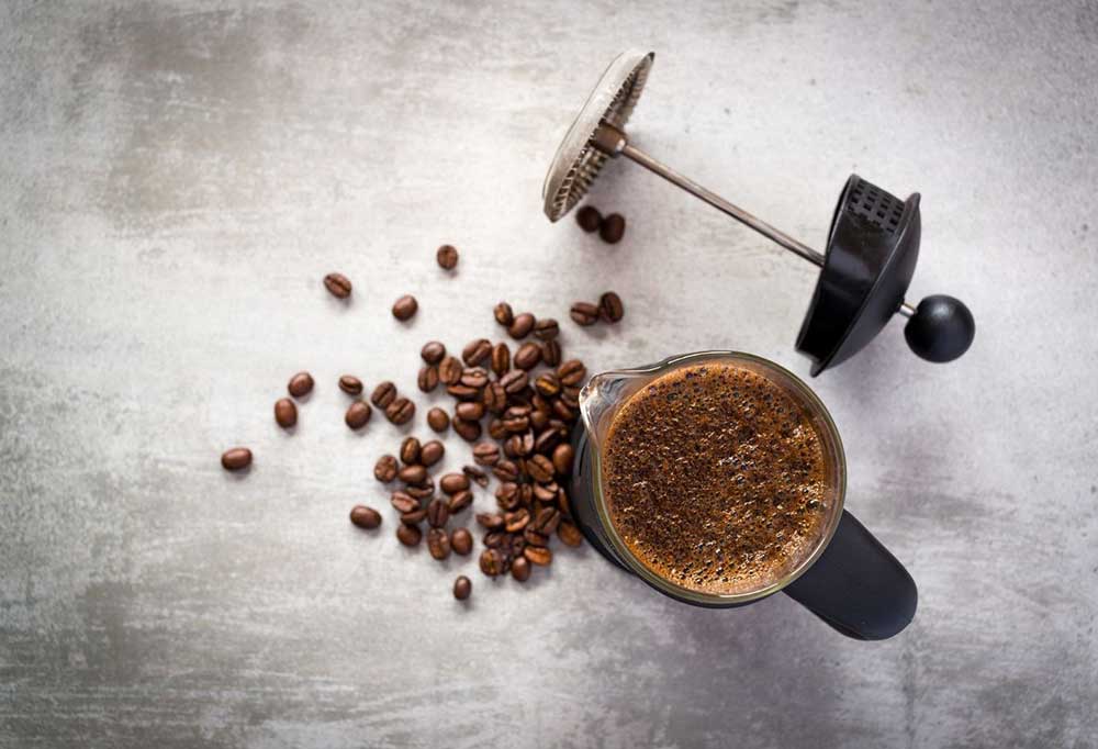 A top view of a French press filled with a coffee beside fresh coffee beans