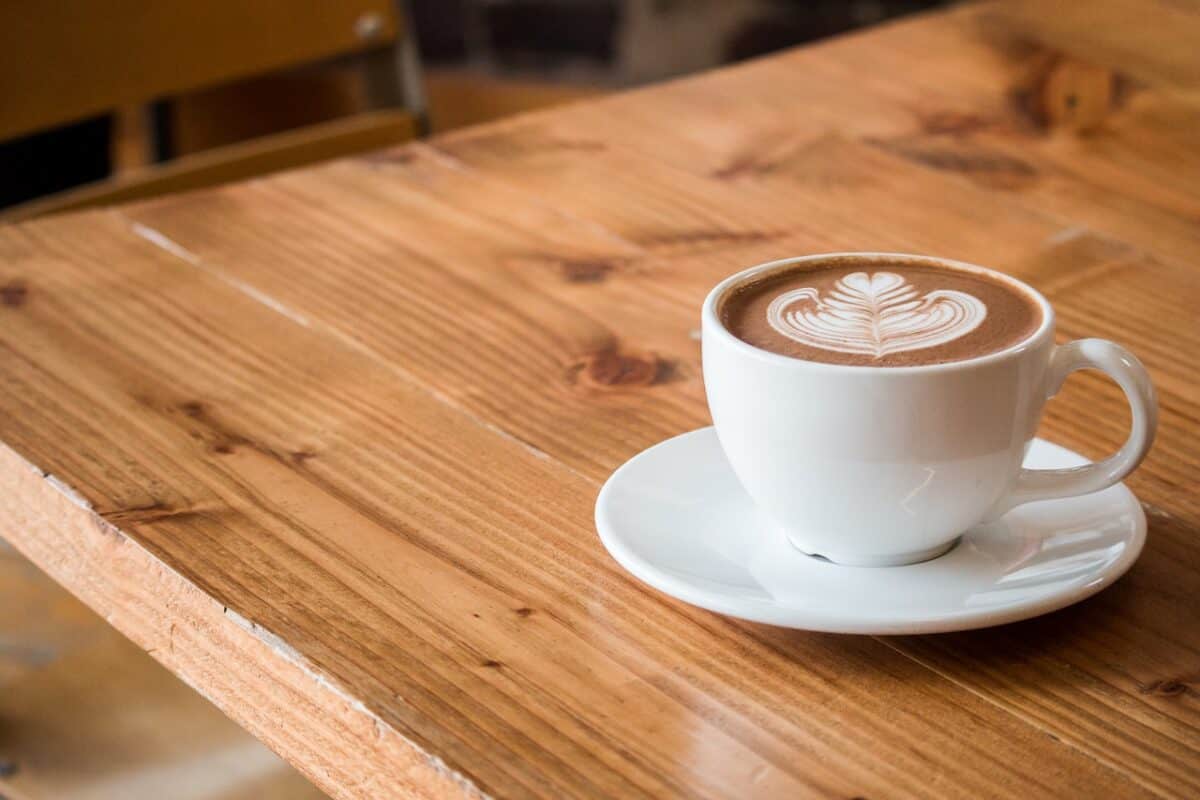 A cup of cappuccino with coffee art on a white saucer placed on a wooden table