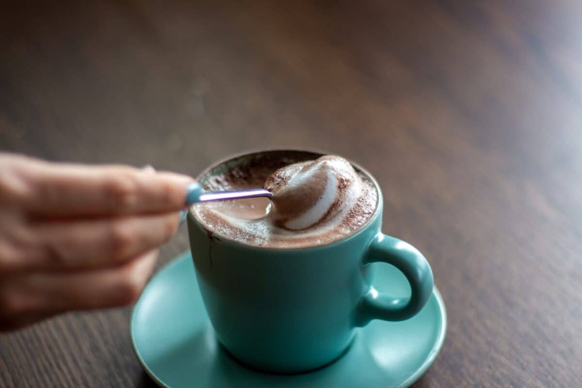 A mug with green color filled with foamy coffee was placed on a green saucer