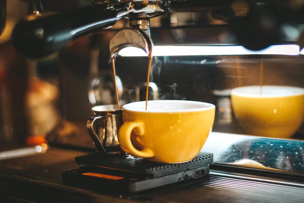 An espresso machine dispensing coffee on two mugs in yellow and silver-gray metal