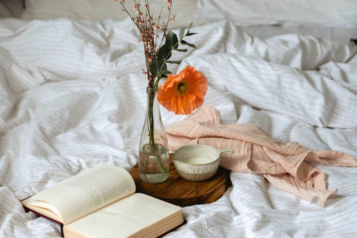 A white cup filled with black coffee beside a cup filled with milk and a clear flower vase on a brown wooden chopping board