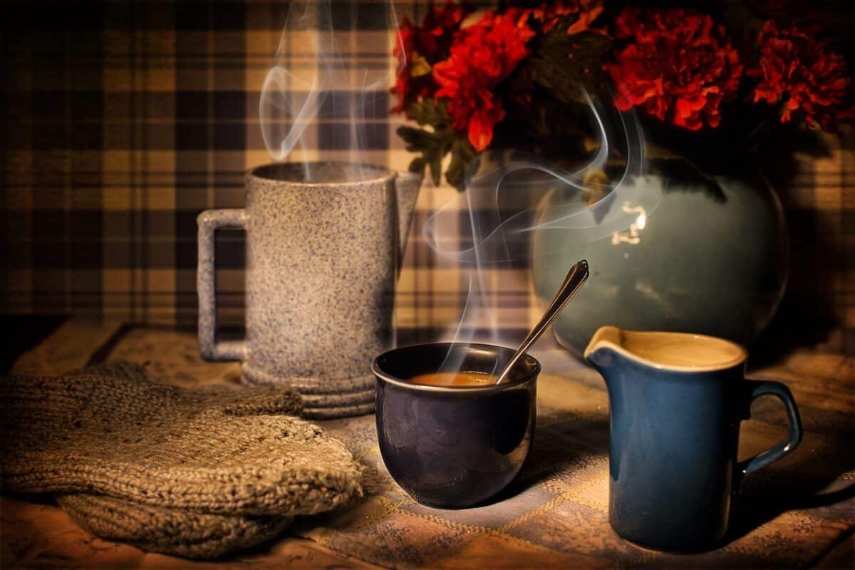 Three different cups of hot coffee beside a vase with red flowers