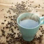 Hot black coffee in a blue cup surrounded by coffee beans is placed on a brown rattan