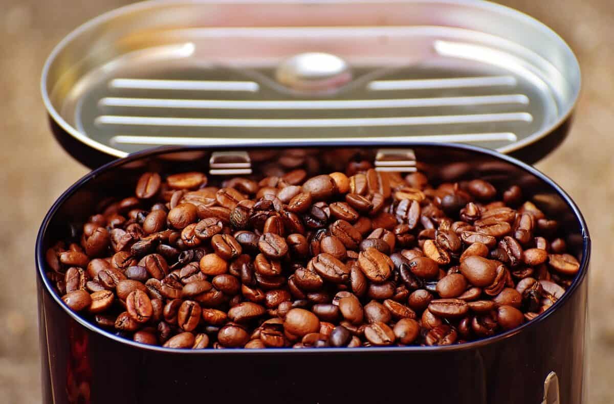 A purple oval-shaped tin can filled with roasted coffee beans