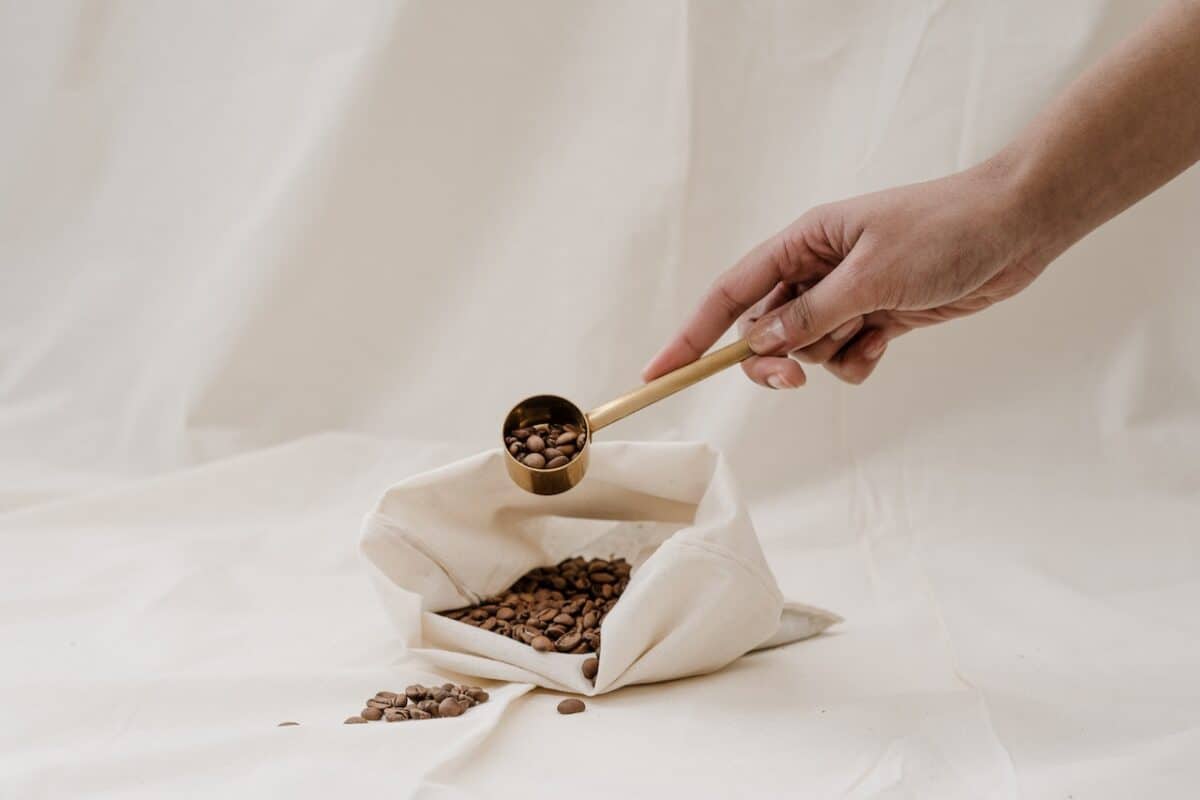 Hand holding a scoop full of coffee beans placed on a white cloth bag