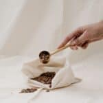 Hand holding a scoop full of coffee beans placed on a white cloth bag