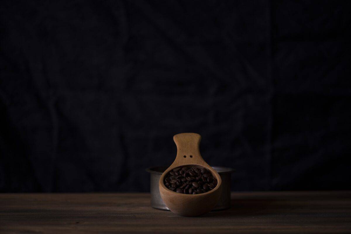 A wooden scoop filled with coffee beans placed on a wooden table