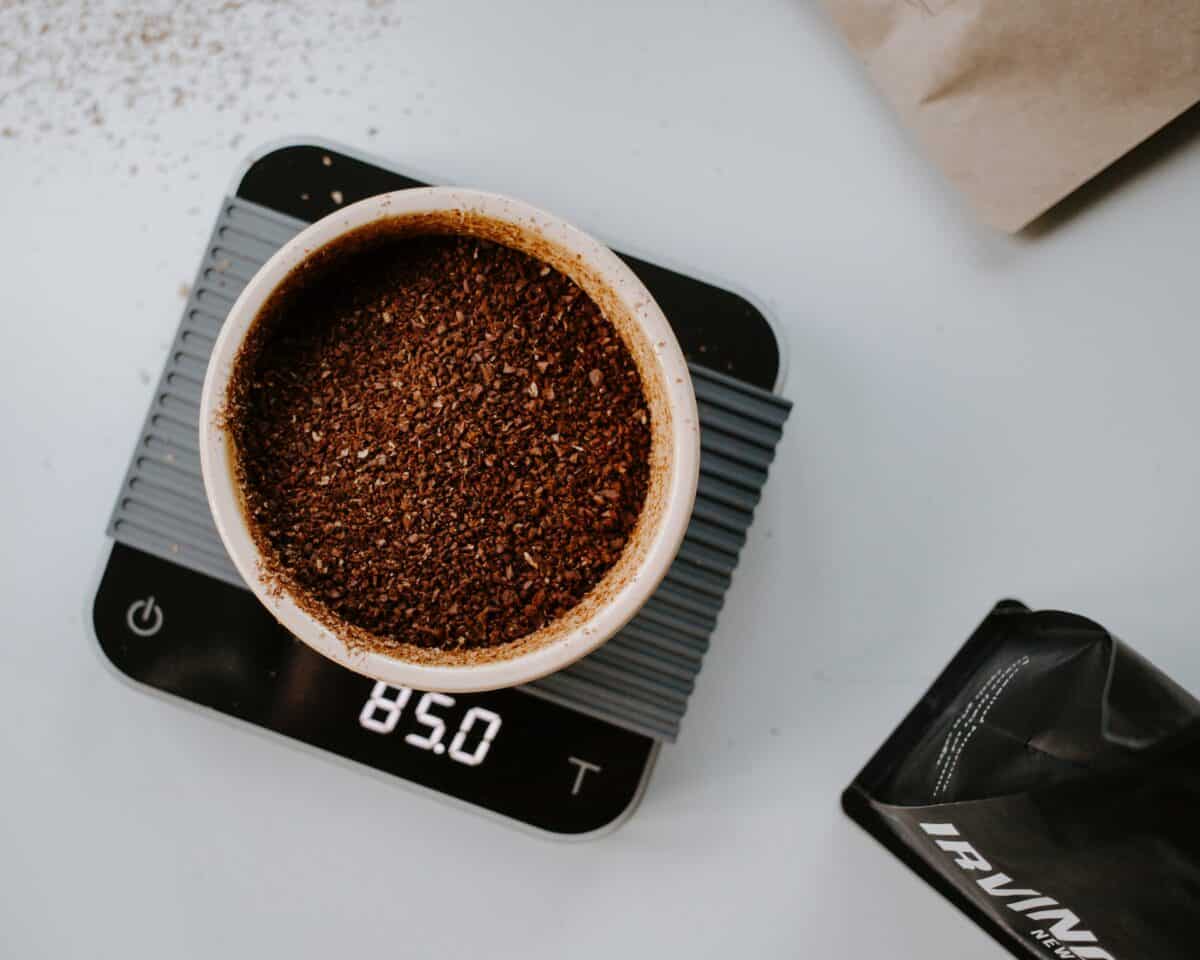 A top view of grind coffee bean placed on a white bowl being weighed on a black weighing scale