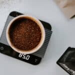 A top view of grind coffee bean placed on a white bowl being weighed on a black weighing scale