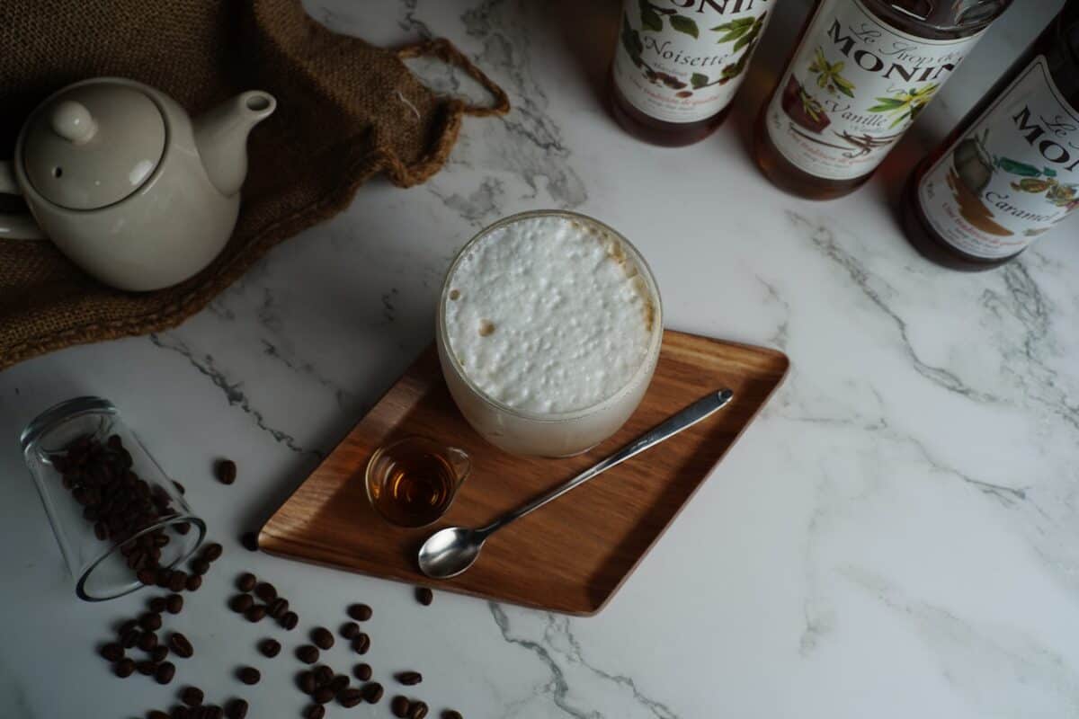 Fresh coffee beans tipped over a clear glass with a glass of coffee frappe beside it