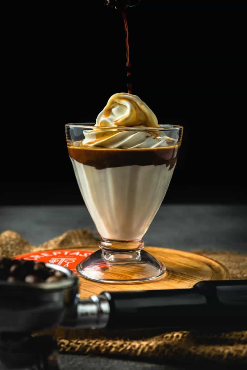 Clear glass with an ice-cream sundae being poured of coffee syrup placed on brown wood
