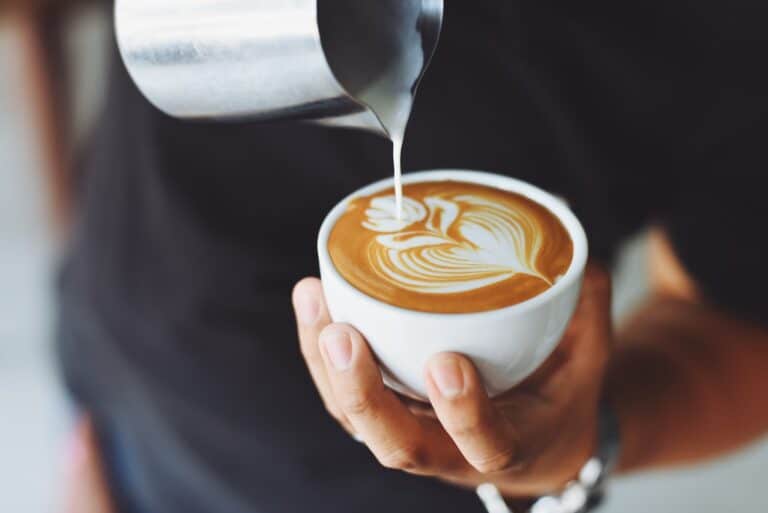 A person in a black shirt making coffee art on a cup of coffee