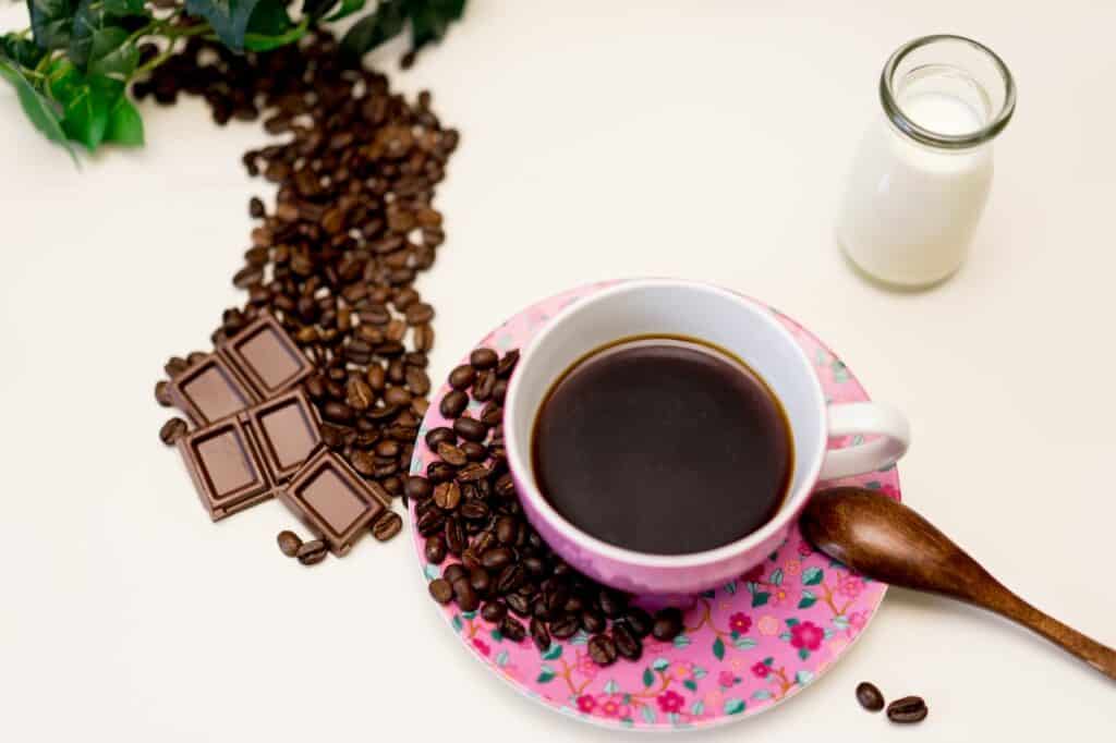 A cup of coffee was placed on a floral saucer beside coffee beans and chocolate