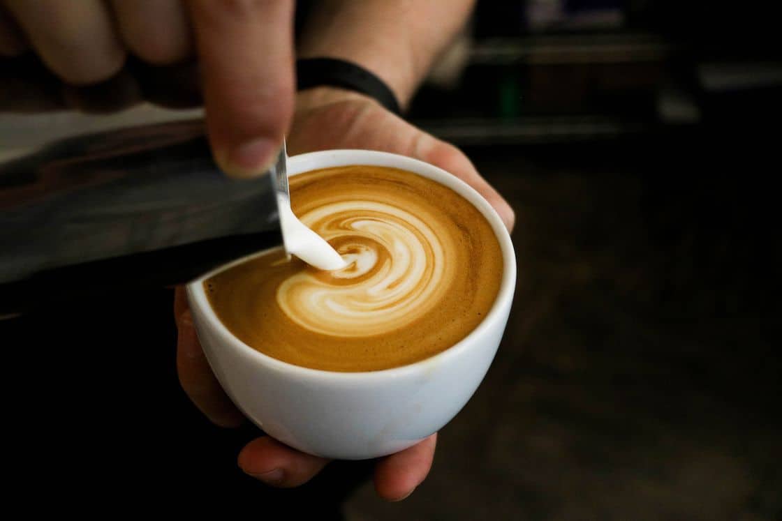 Barista pouring steamed milk on a cup filled with espresso