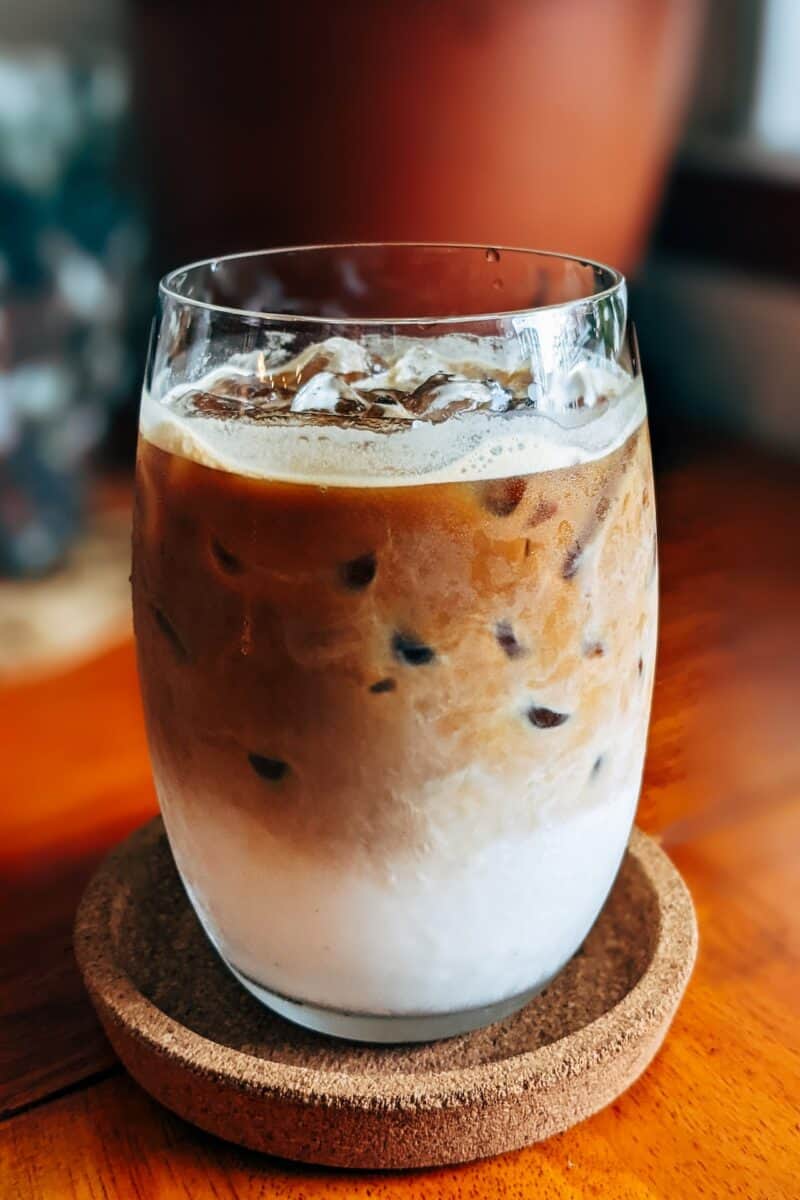 A clear glass filled with iced coffee was placed on a brown saucer