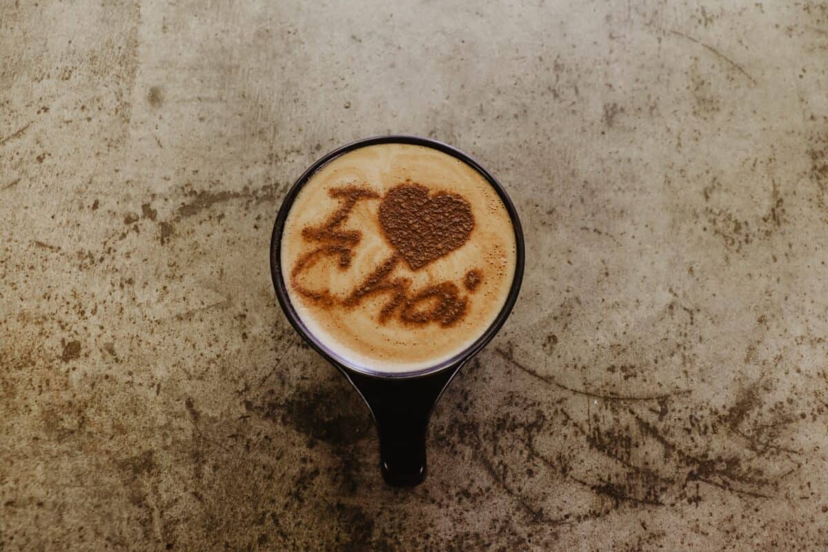 A brown 'I heart chai' coffee art on top of a chai latte on a black mug