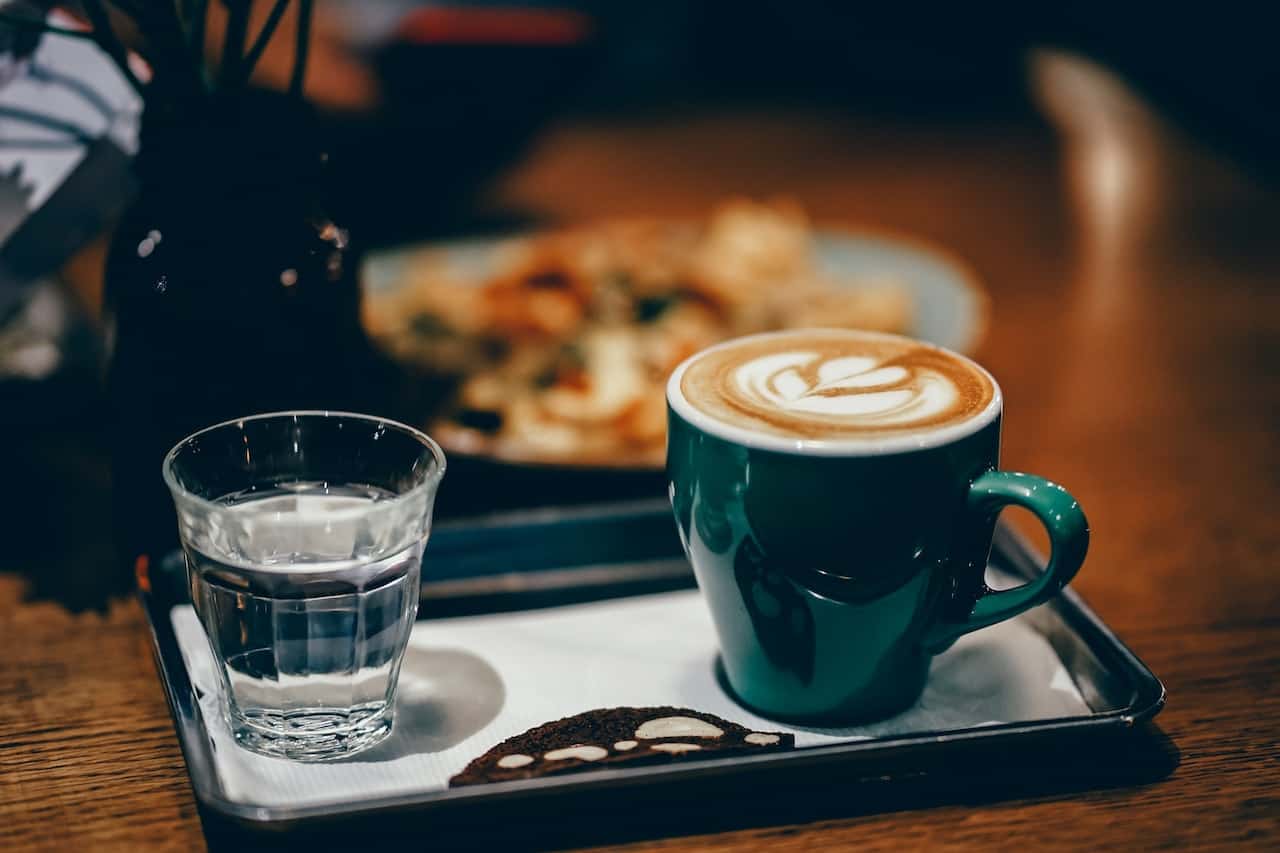 A green mug filled with foamy latte beside a cup of water